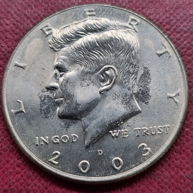 2003 Kennedy half dollar struck-through error showing depression void in Kennedy portrait where foreign material interrupted the strike